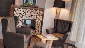A cozy seating area with two leather armchairs and a small wooden table, a fireplace with a log wall, and a lamp on the wall.