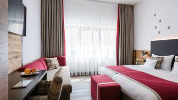 Een moderne hotelkamer met een bed, een bureau met een laptop, een stoel, een bank en een groot raam met gordijnen.