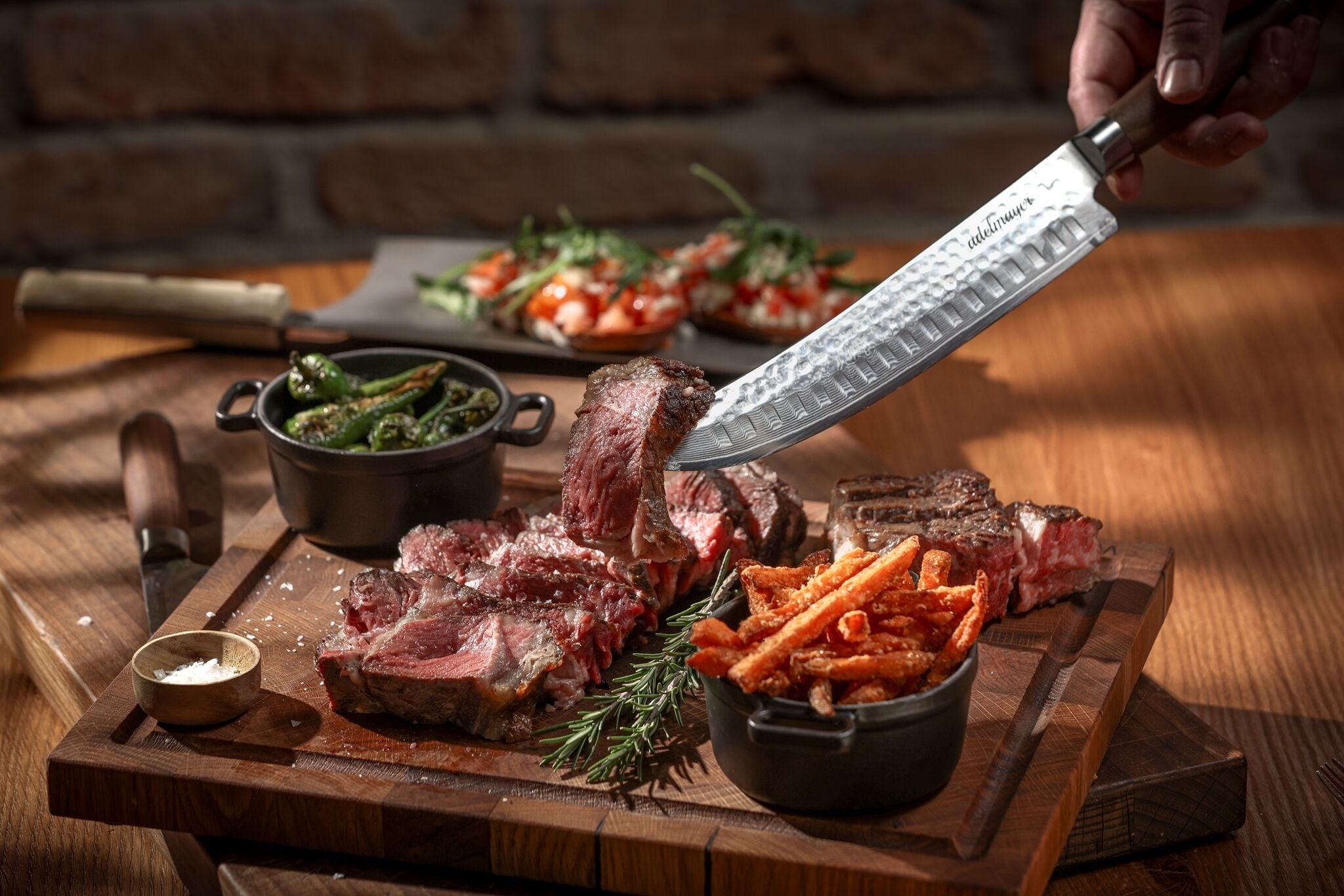 A wooden cutting board with sliced steak, fries, and a small bowl of seasoning.