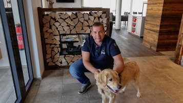 Ein Mann sitzt mit einem Hund in einem Raum mit Holzboden, Kamin und Fernseher an der Wand.