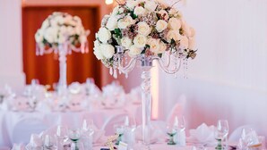 Une salle de banquet avec des tables rondes dressées pour un événement formel, agrémentée de compositions florales et de verres en cristal.