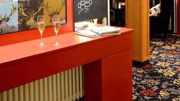 A reception desk with a chalkboard menu, two glasses of wine, and a bookshelf in the background.