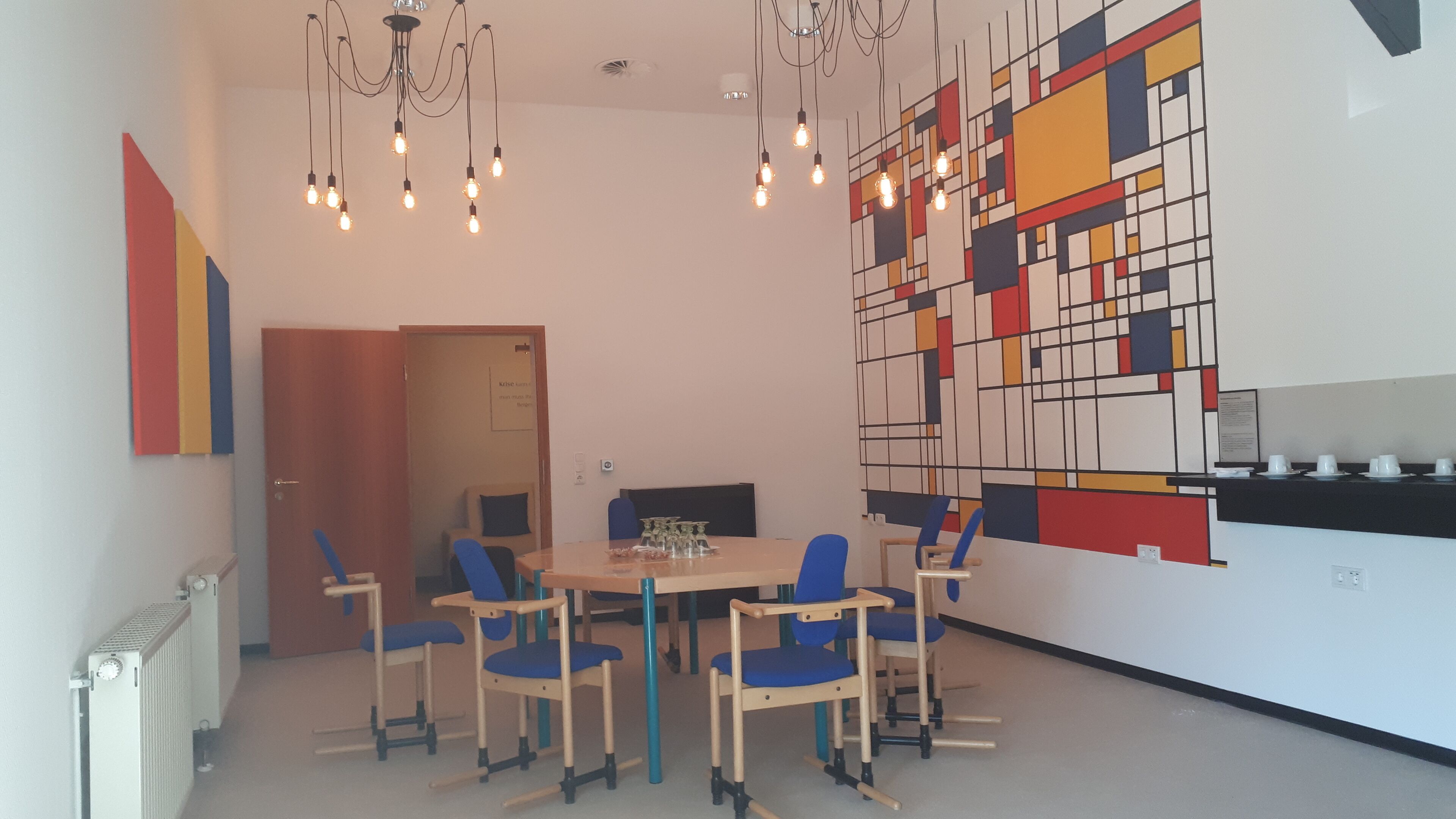 A modern dining area with a round table, blue chairs, and a colorful abstract wall art.