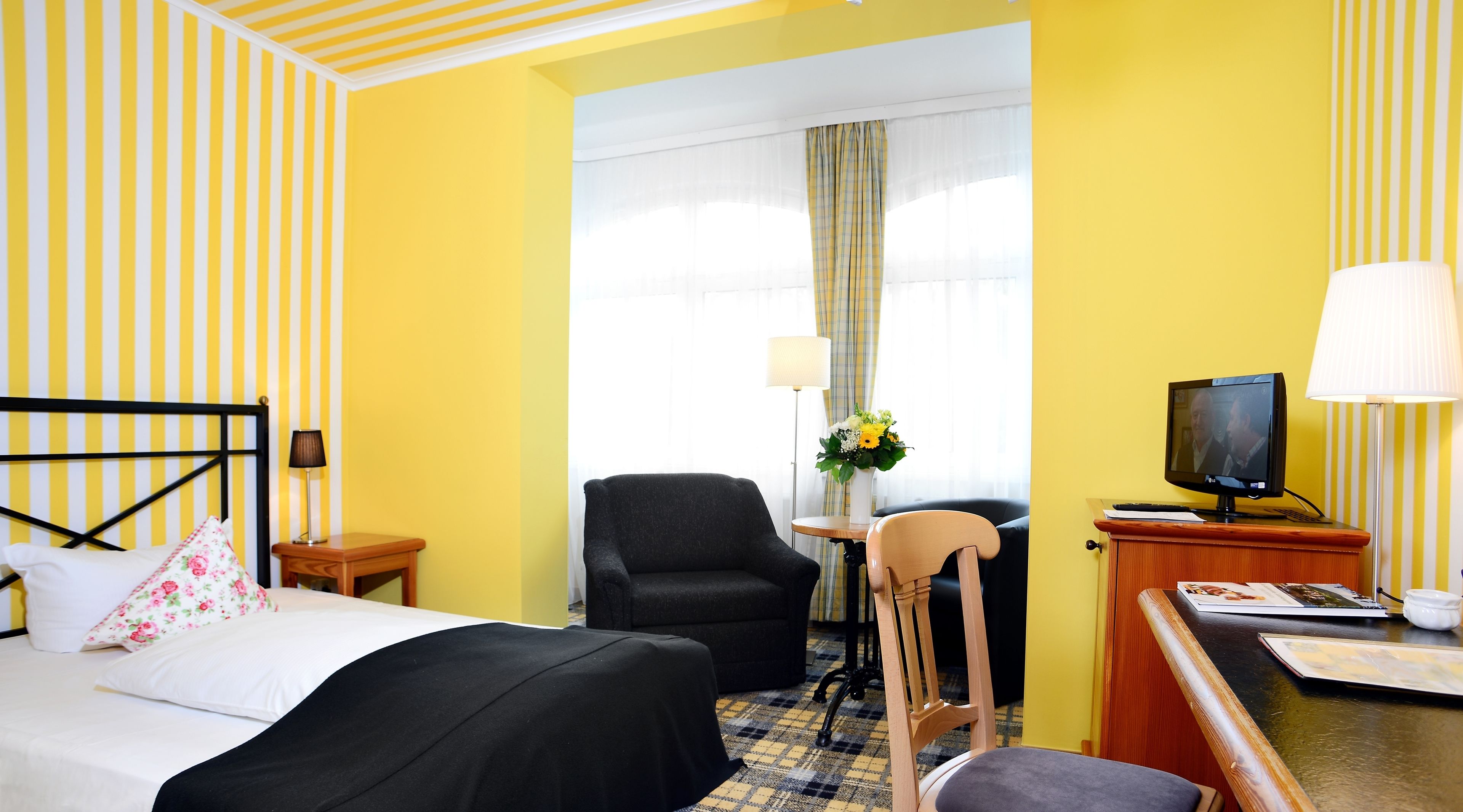 Habitación de hotel con cama, escritorio con televisor, silla y ventana con cortinas.