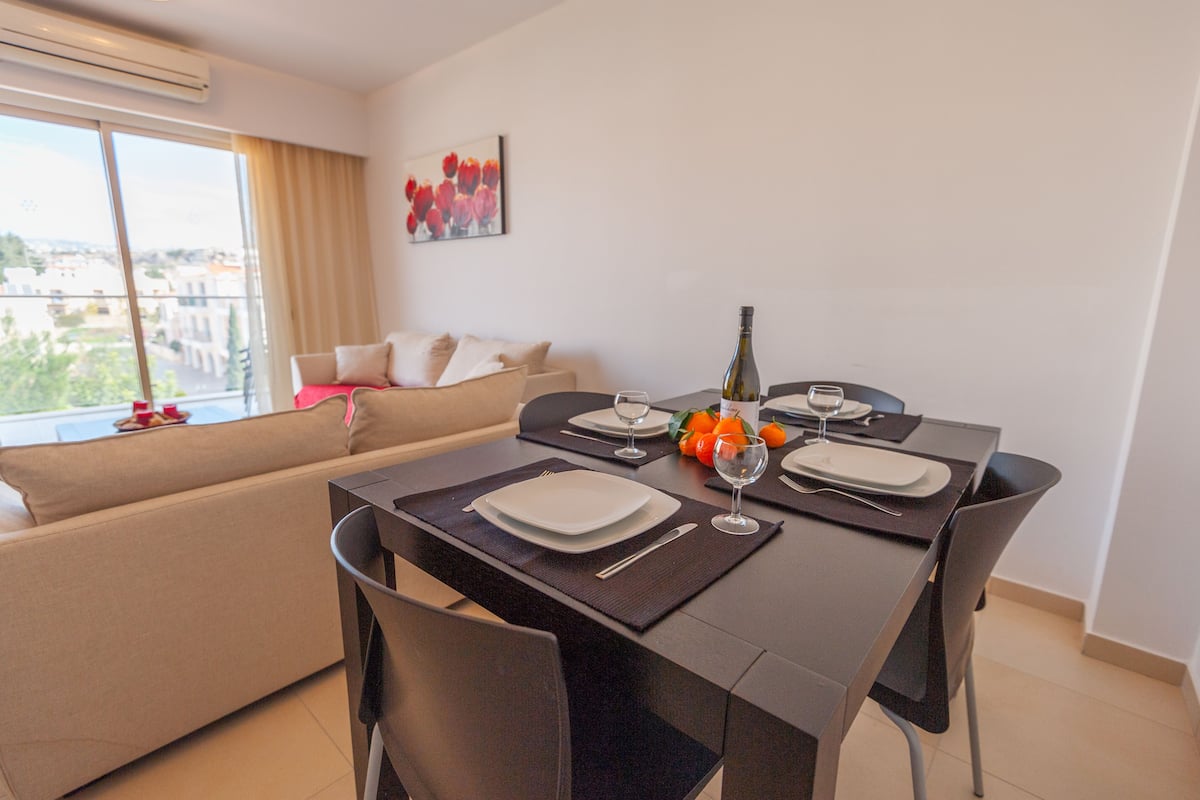 Un comedor con una mesa dispuesta para dos personas, un sofá y una ventana con vista a la ciudad.
