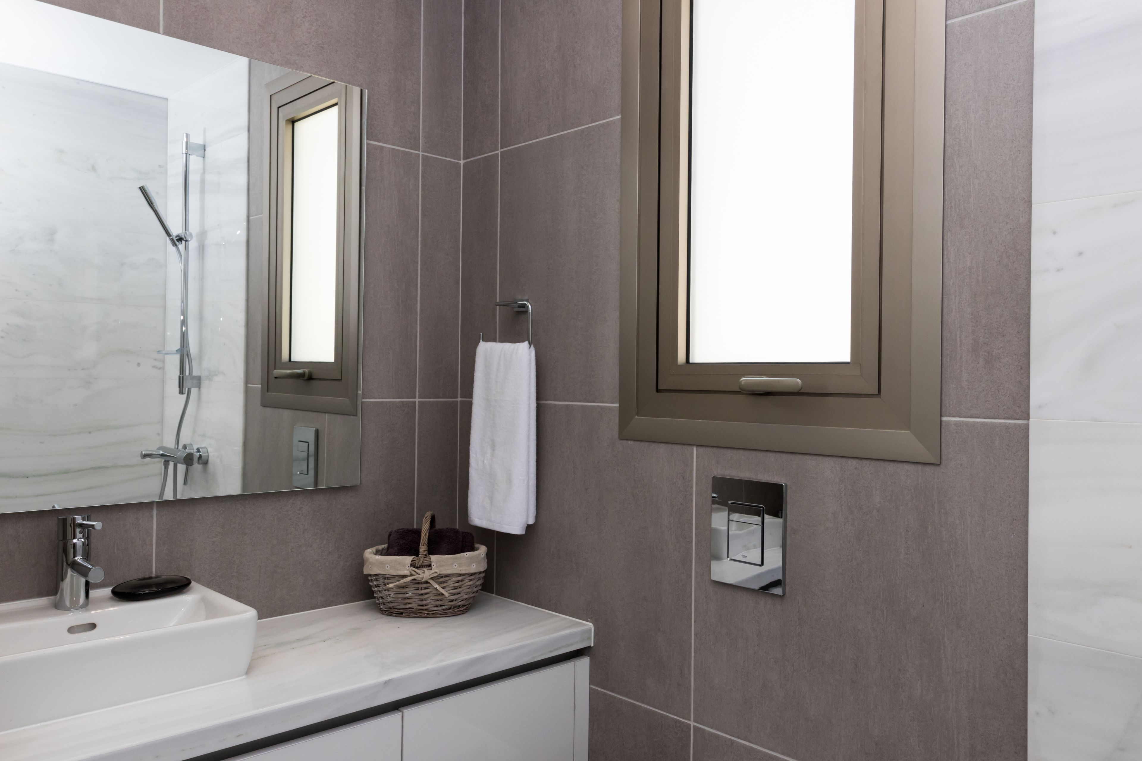 Un baño moderno con un espejo grande, un lavamanos, un perchero para toallas y una ventana.