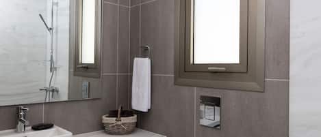 A modern bathroom with a large mirror, a sink, a towel rack, and a window.