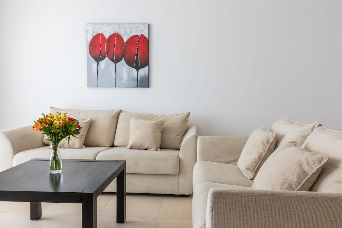 Una sala de estar con un sofá color beige, una mesa de centro de madera oscura y un jarrón con flores.
