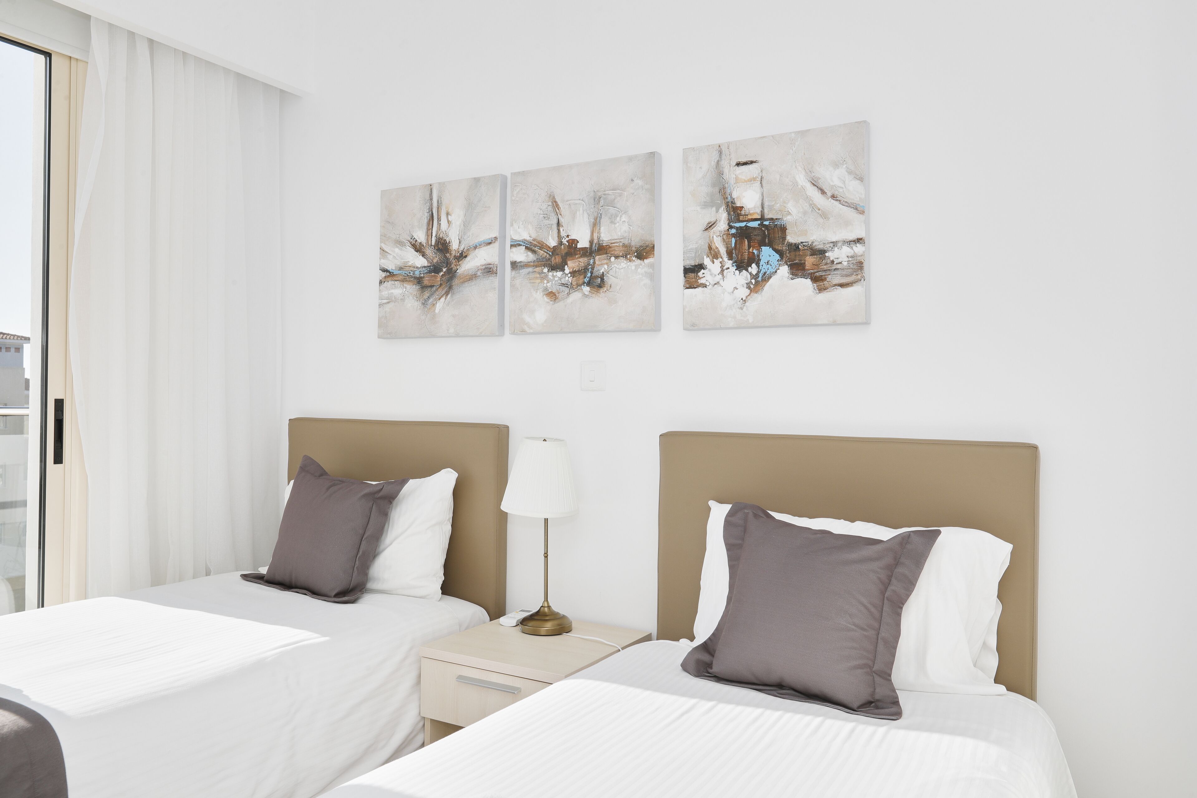 Habitación de hotel con dos camas, una mesita de noche con lámpara y arte abstracto en la pared.