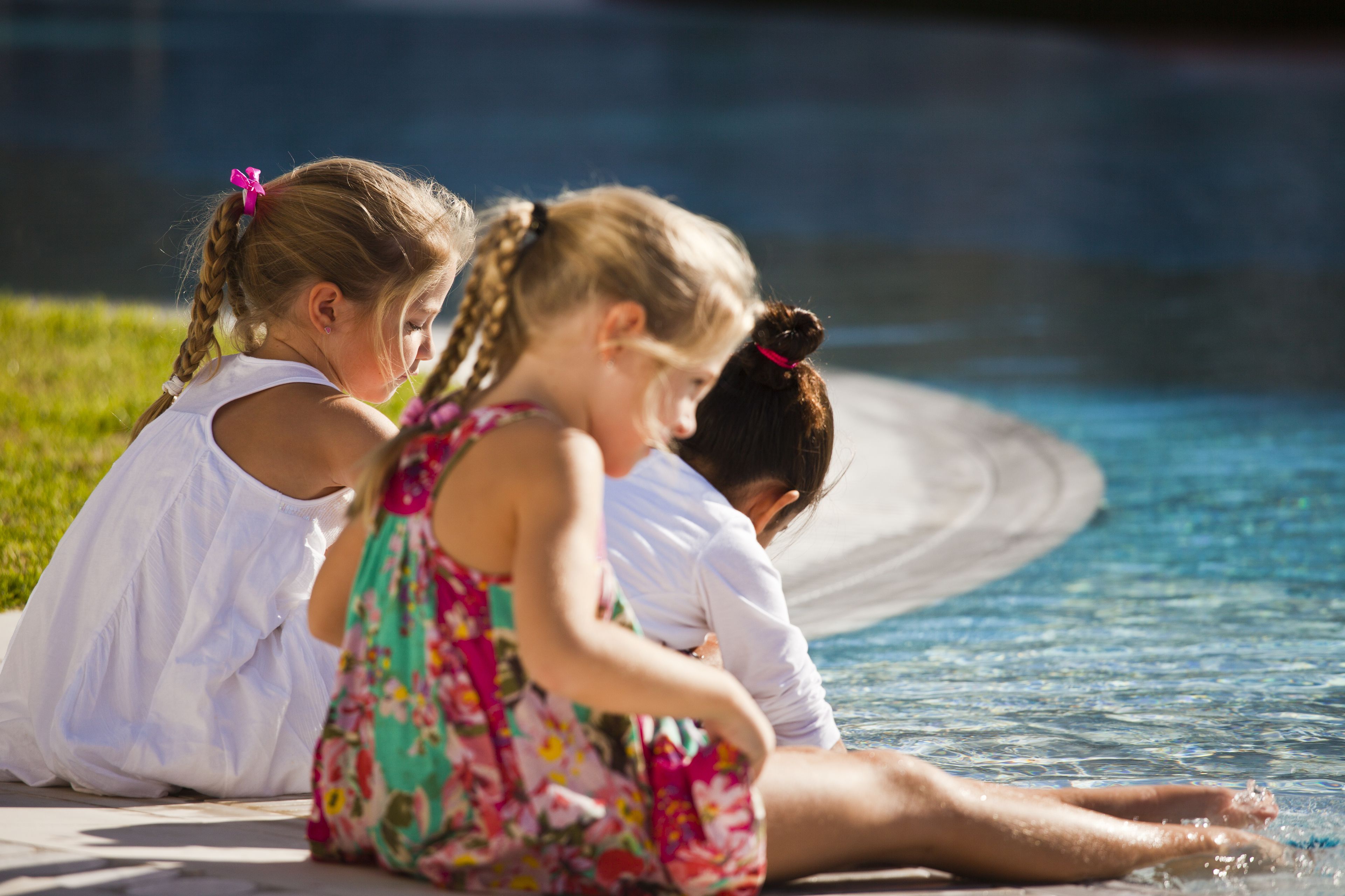 Three children sitting by a poolside.