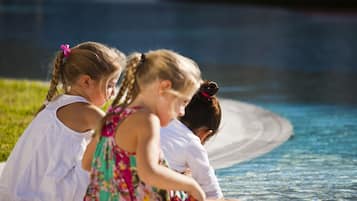 Three children sitting by a poolside.