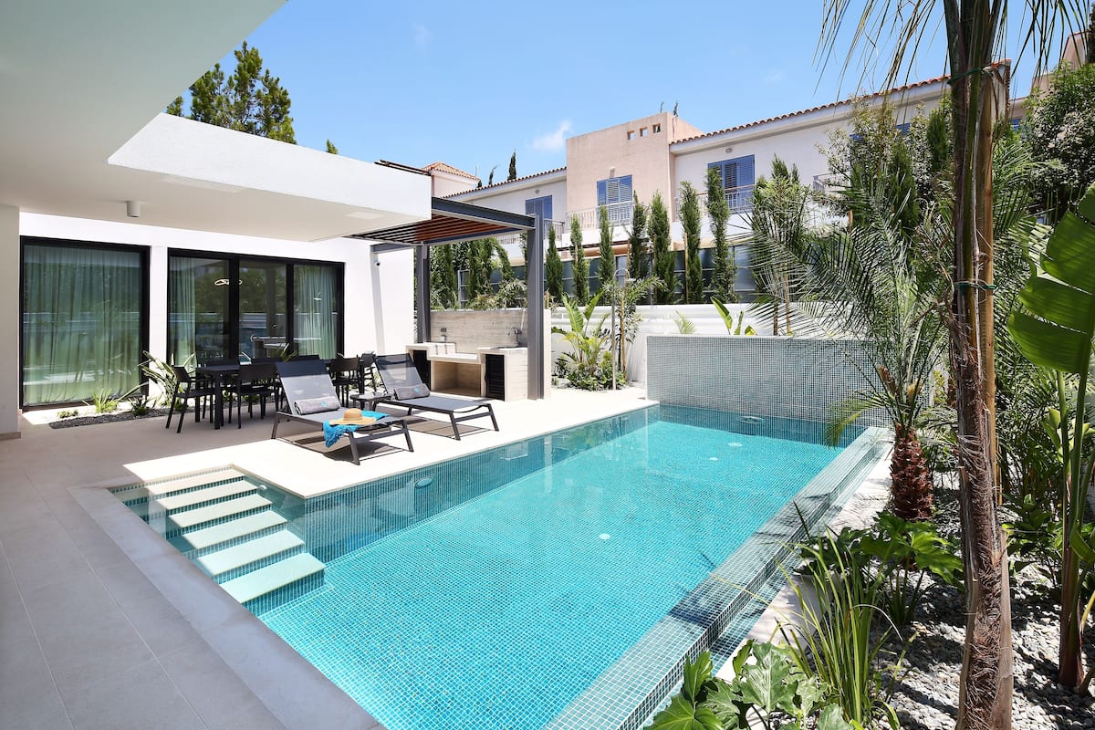 Piscina exterior moderna con escalones de acceso, rodeada por un patio amueblado y vistas a edificios cercanos.