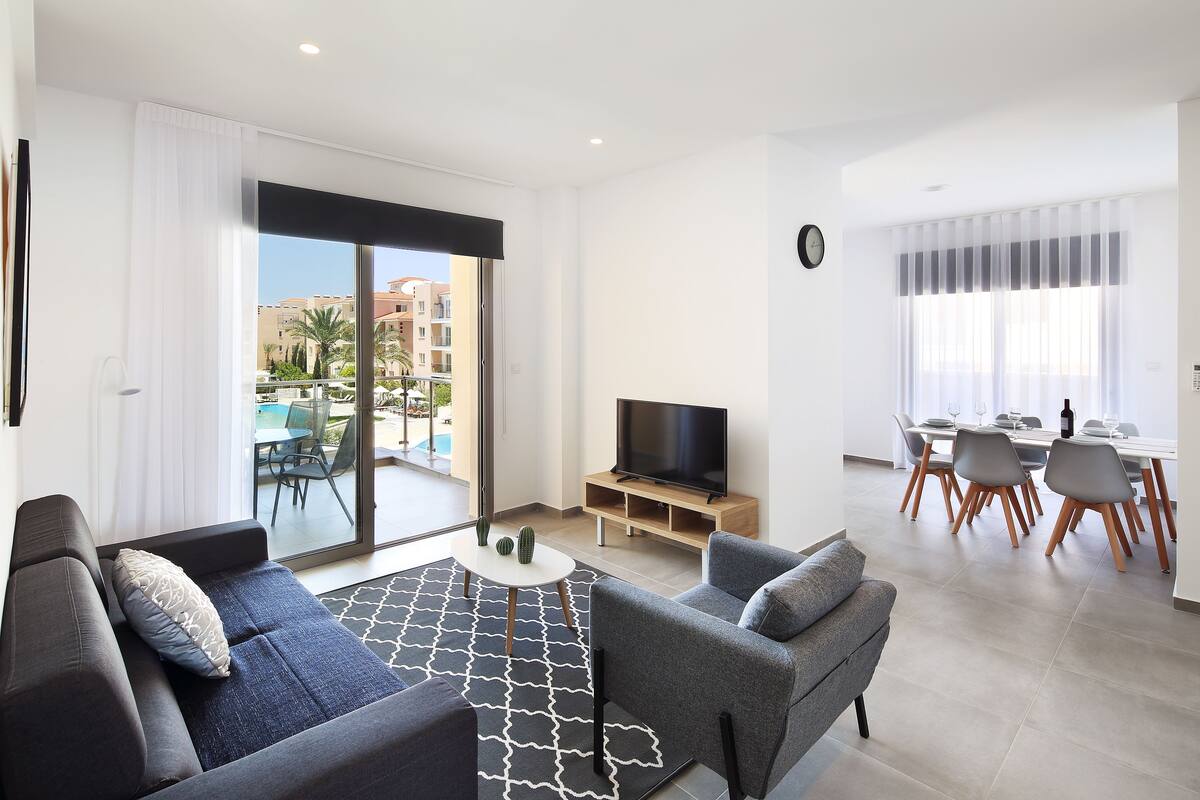 Una sala de estar moderna con sofá, televisor y comedor con sillas y una mesa.