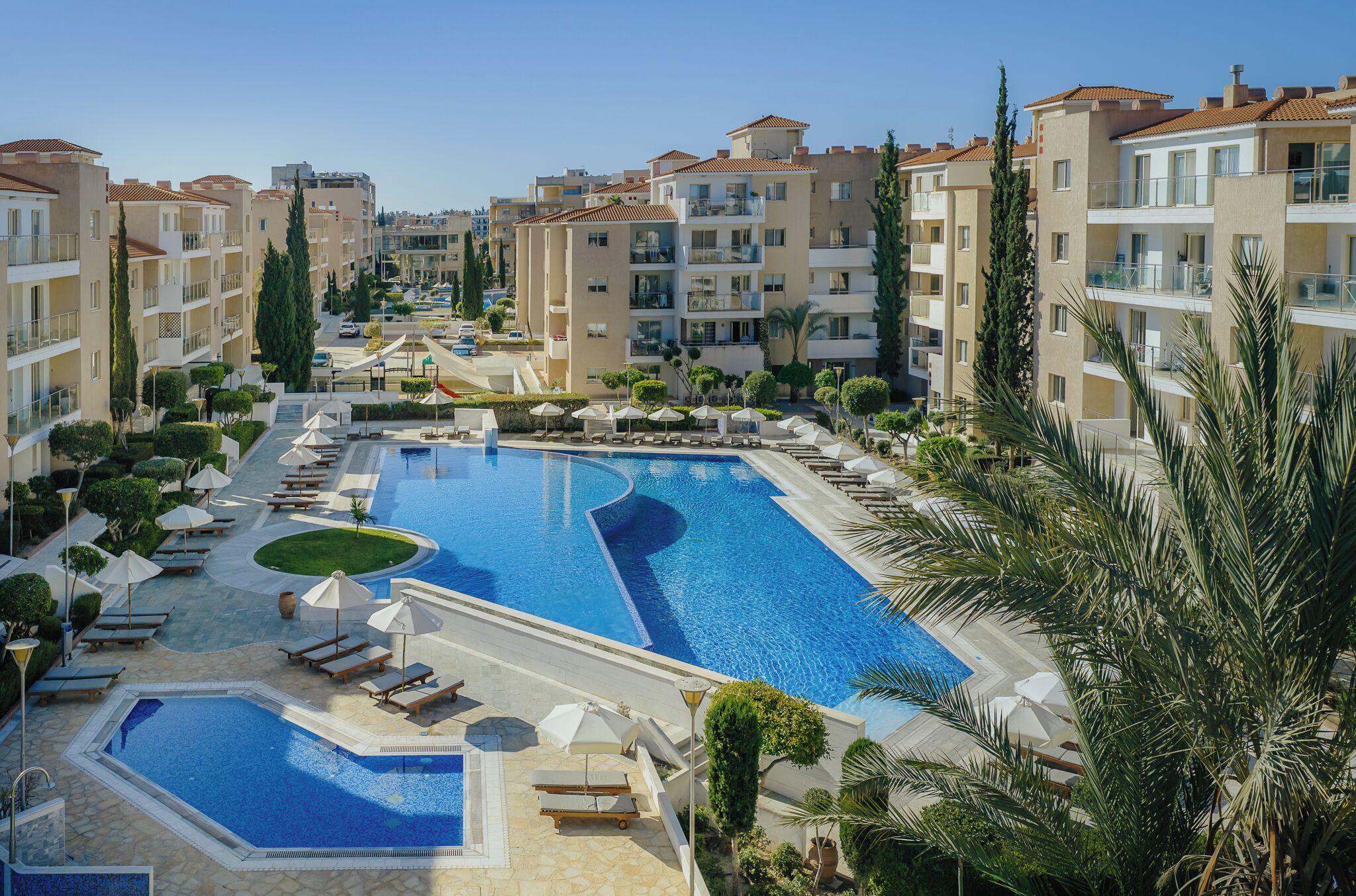 Ein Resort mit mehreren Swimmingpools, Liegestühlen und blauem Himmel.