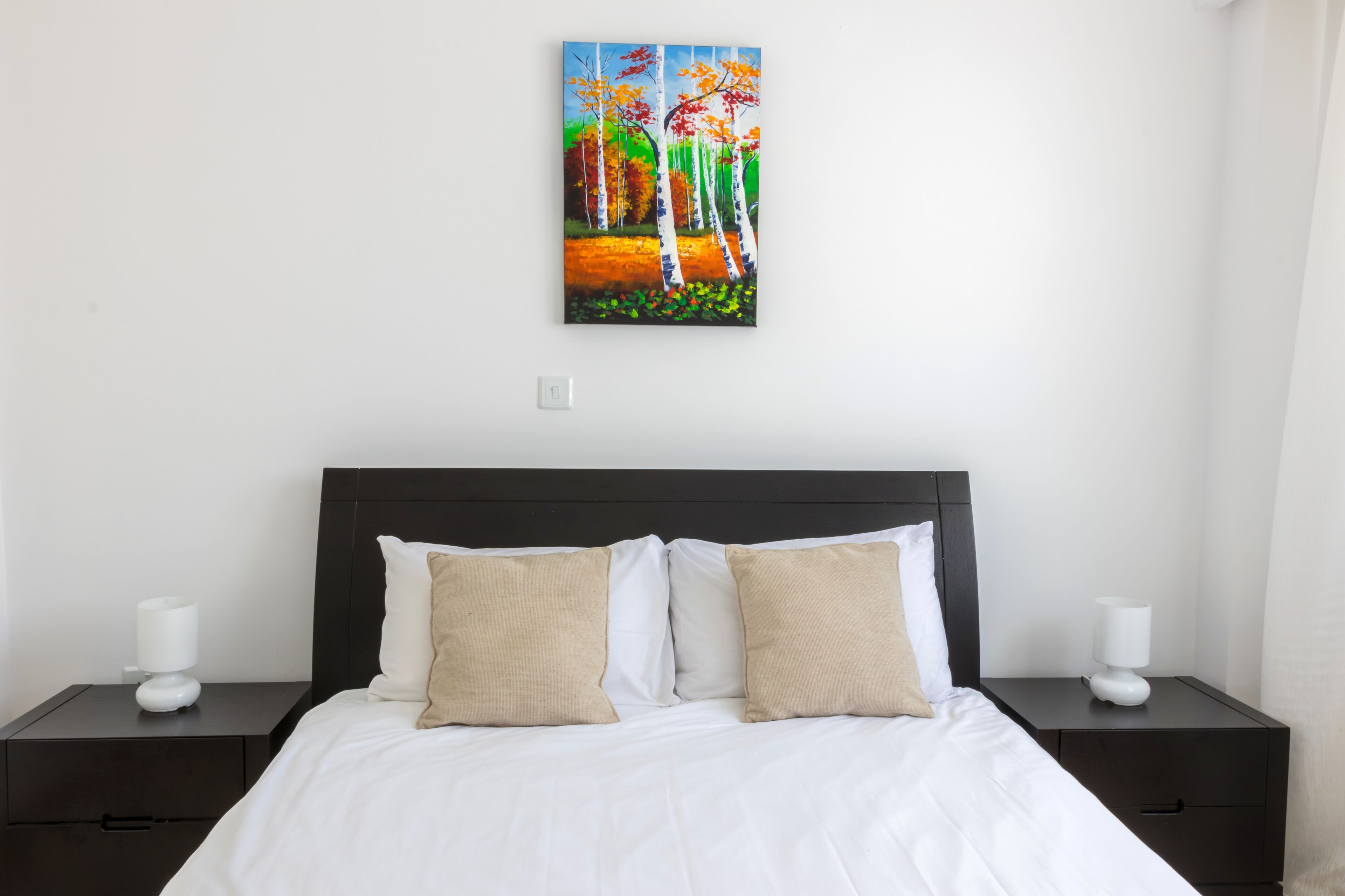 A bedroom with a bed, two bedside tables, and a painting on the wall.