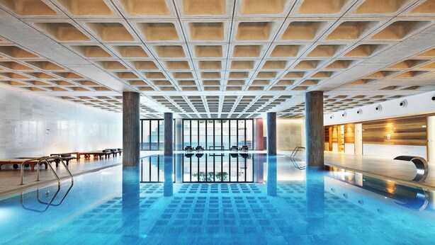 Una piscina interior amplia con techo de diseño cuadriculado y paredes de vidrio transparente.
