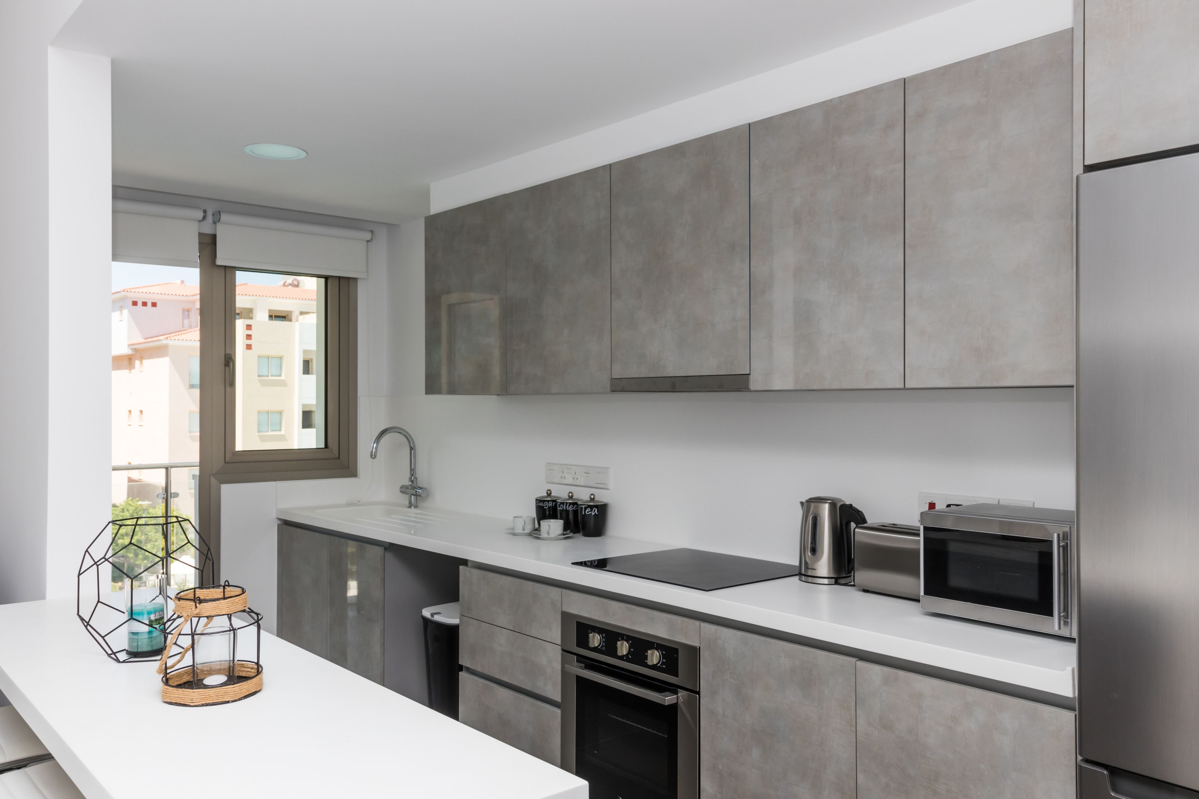 Una cocina moderna con armarios grises, un refrigerador de acero inoxidable, un microondas, una tetera y un horno empotrado.