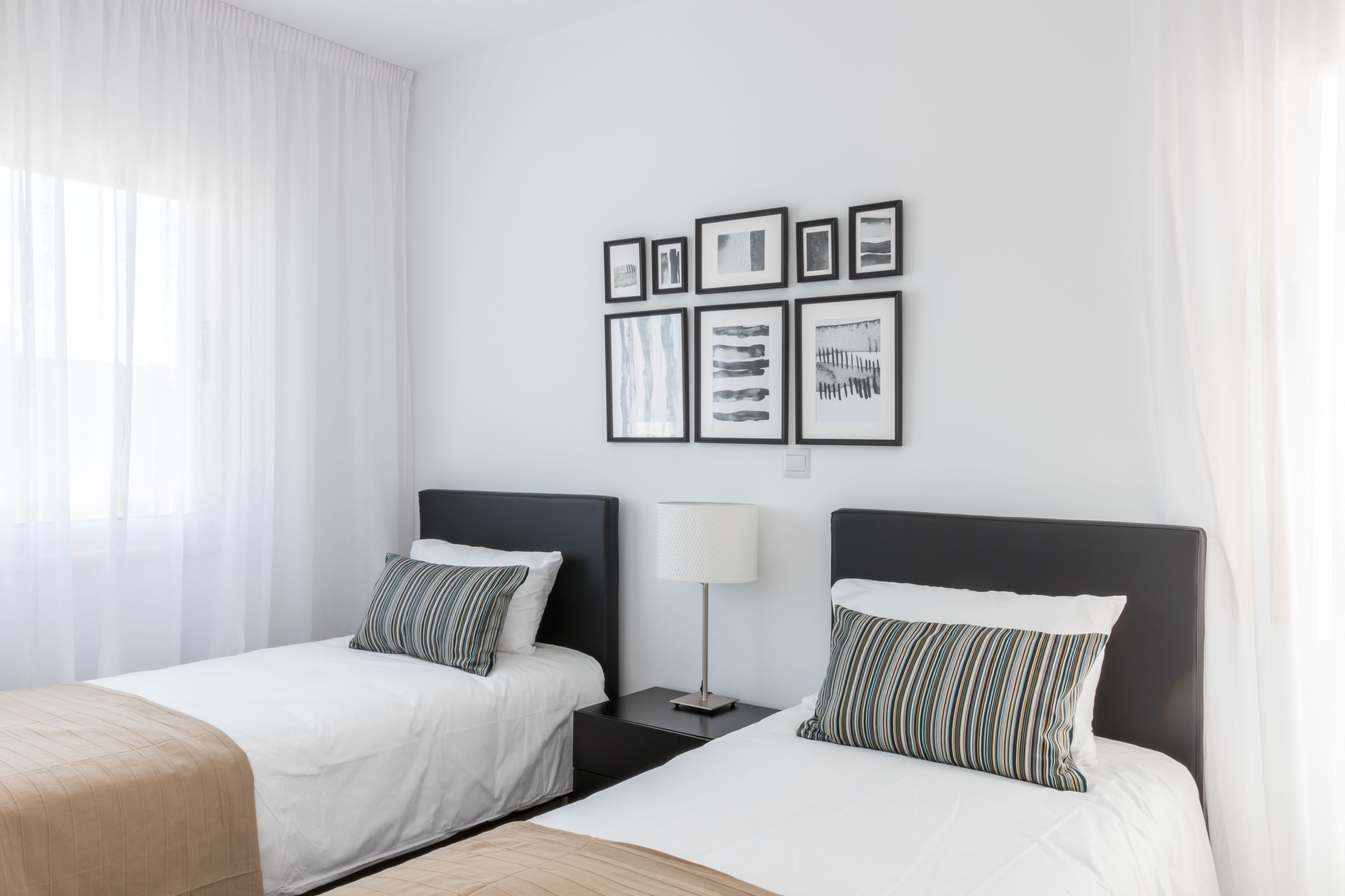 A hotel room with two beds, a nightstand, a lamp, and a wall with framed pictures.