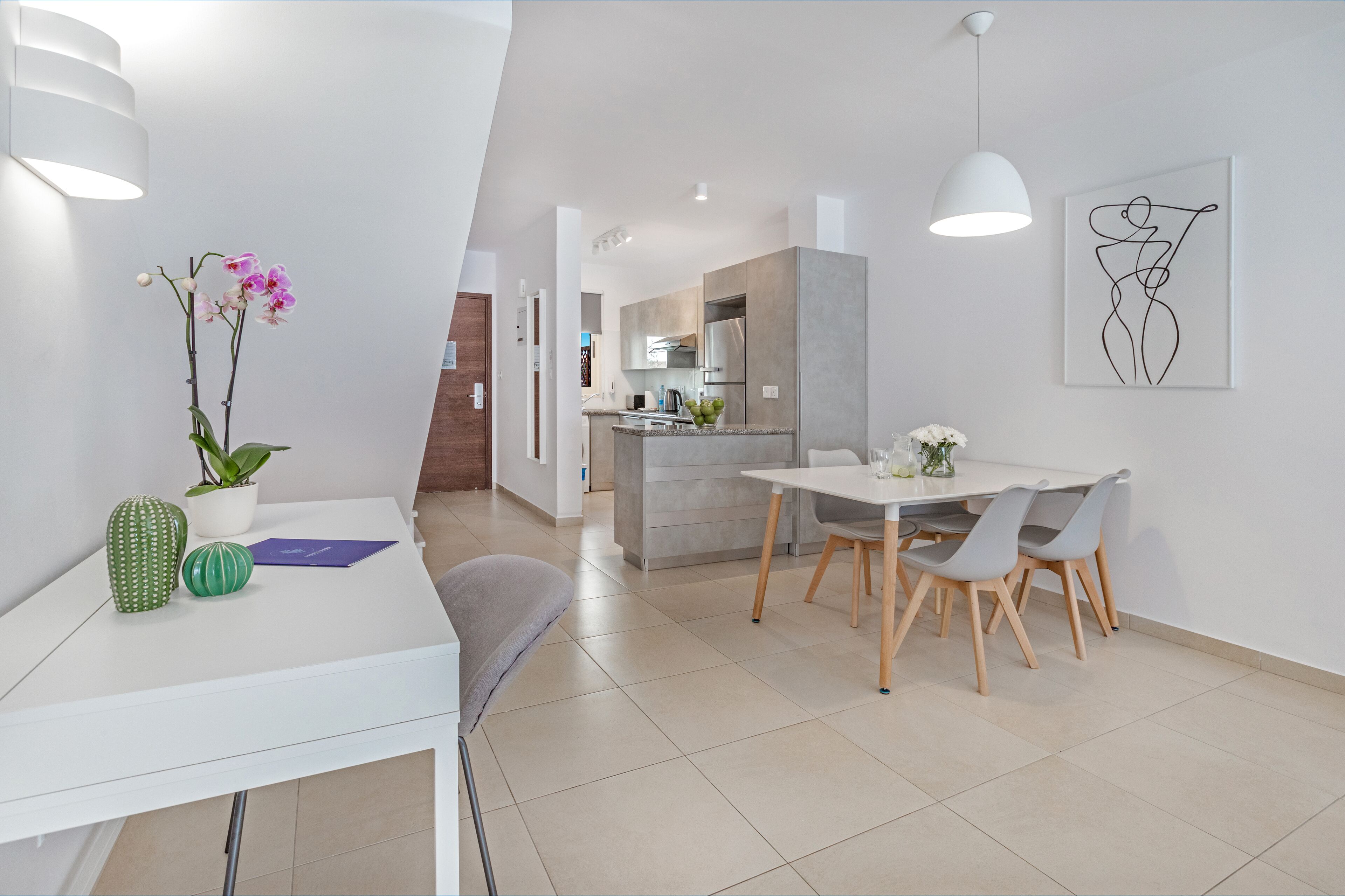 Une cuisine moderne avec des meubles gris, un îlot central et un coin repas comprenant une table blanche et des chaises grises.