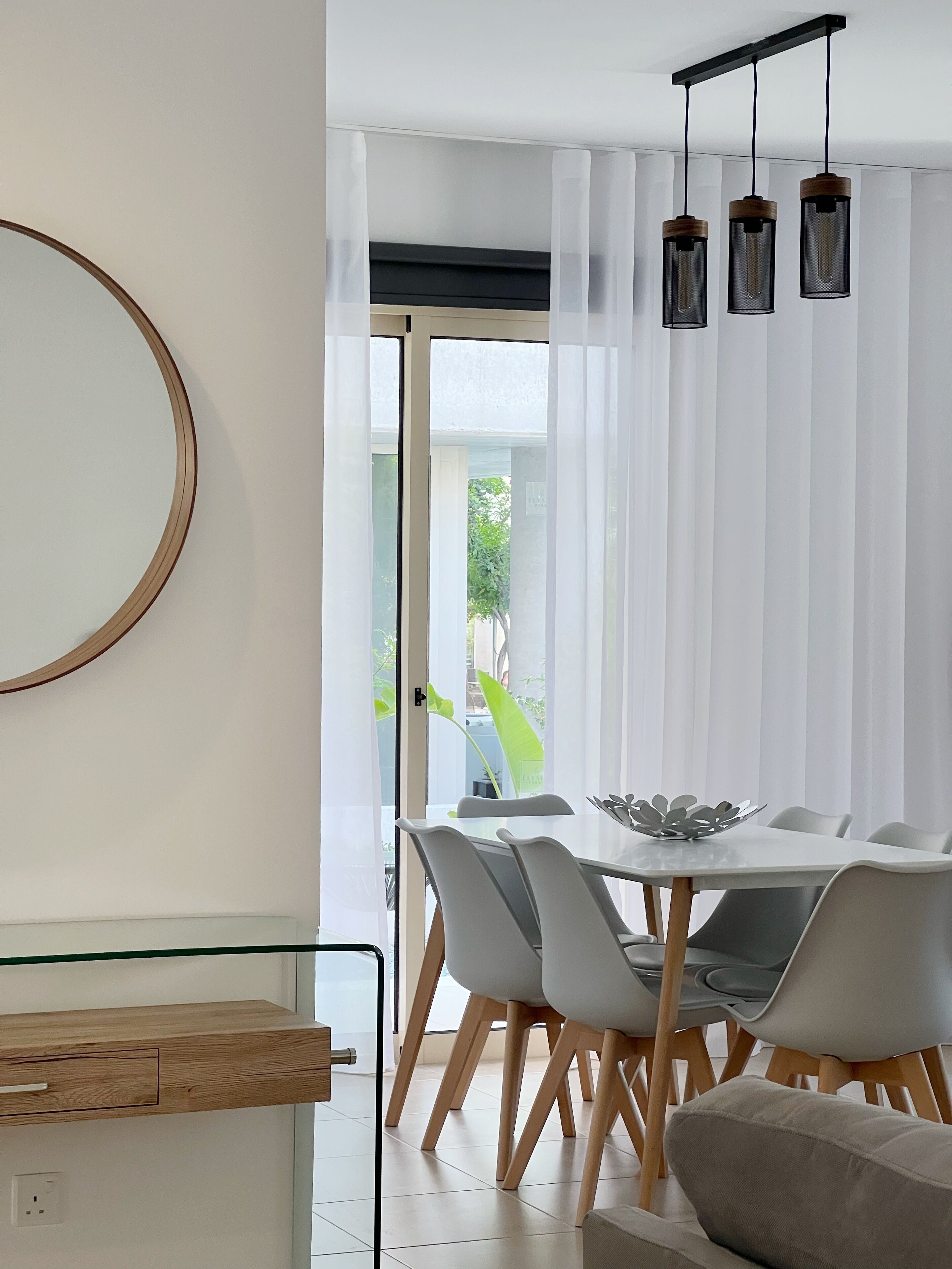 Un espace repas moderne avec une table en verre, des chaises blanches et un buffet en bois.