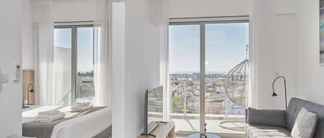 A modern hotel room with a bed, a sofa, a small table, and a view of the city.
