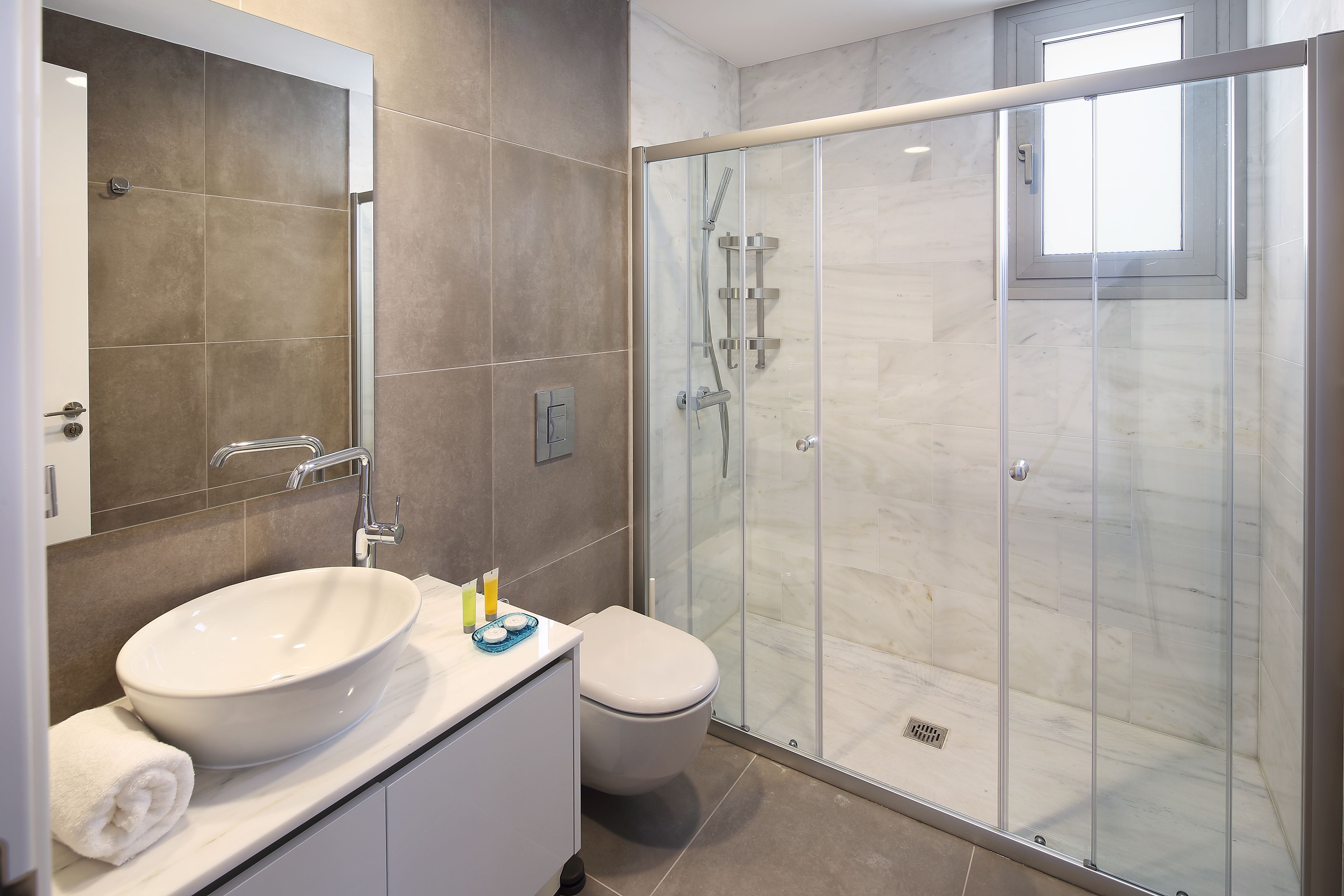 Une salle de bain moderne avec un grand miroir, un lavabo blanc et une douche à parois de verre.