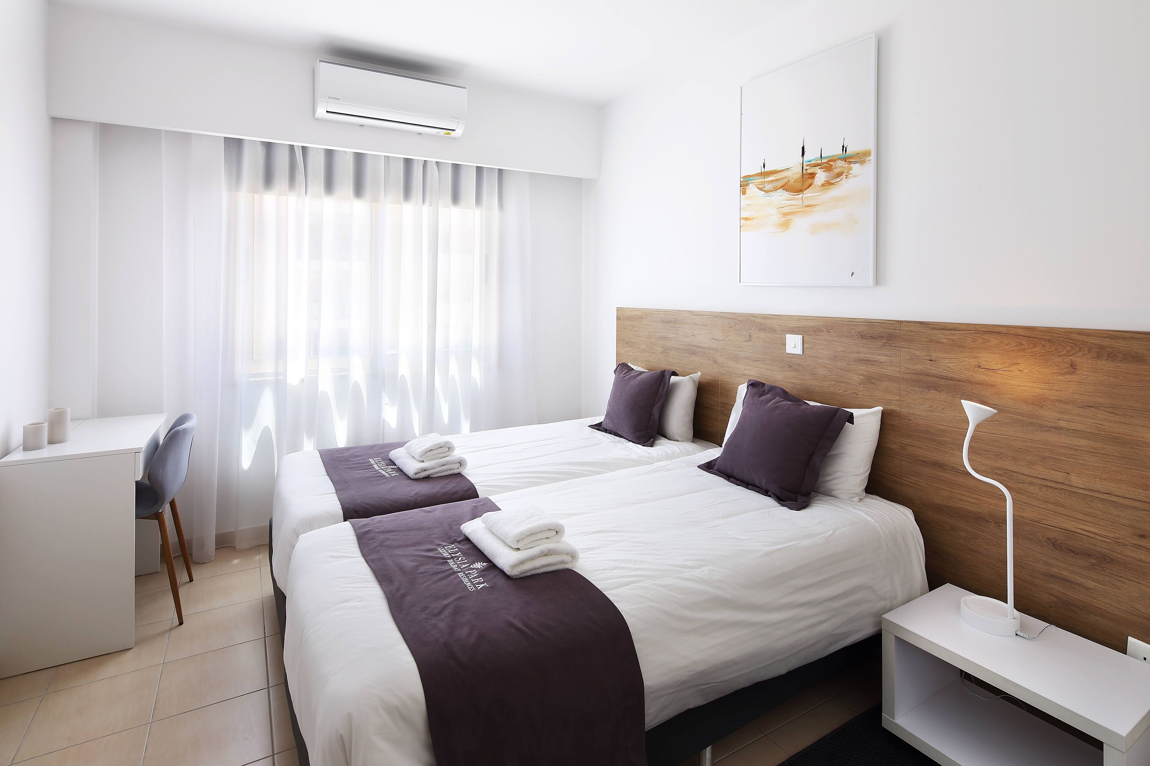 A hotel room with two beds, a desk, and a modern lamp.