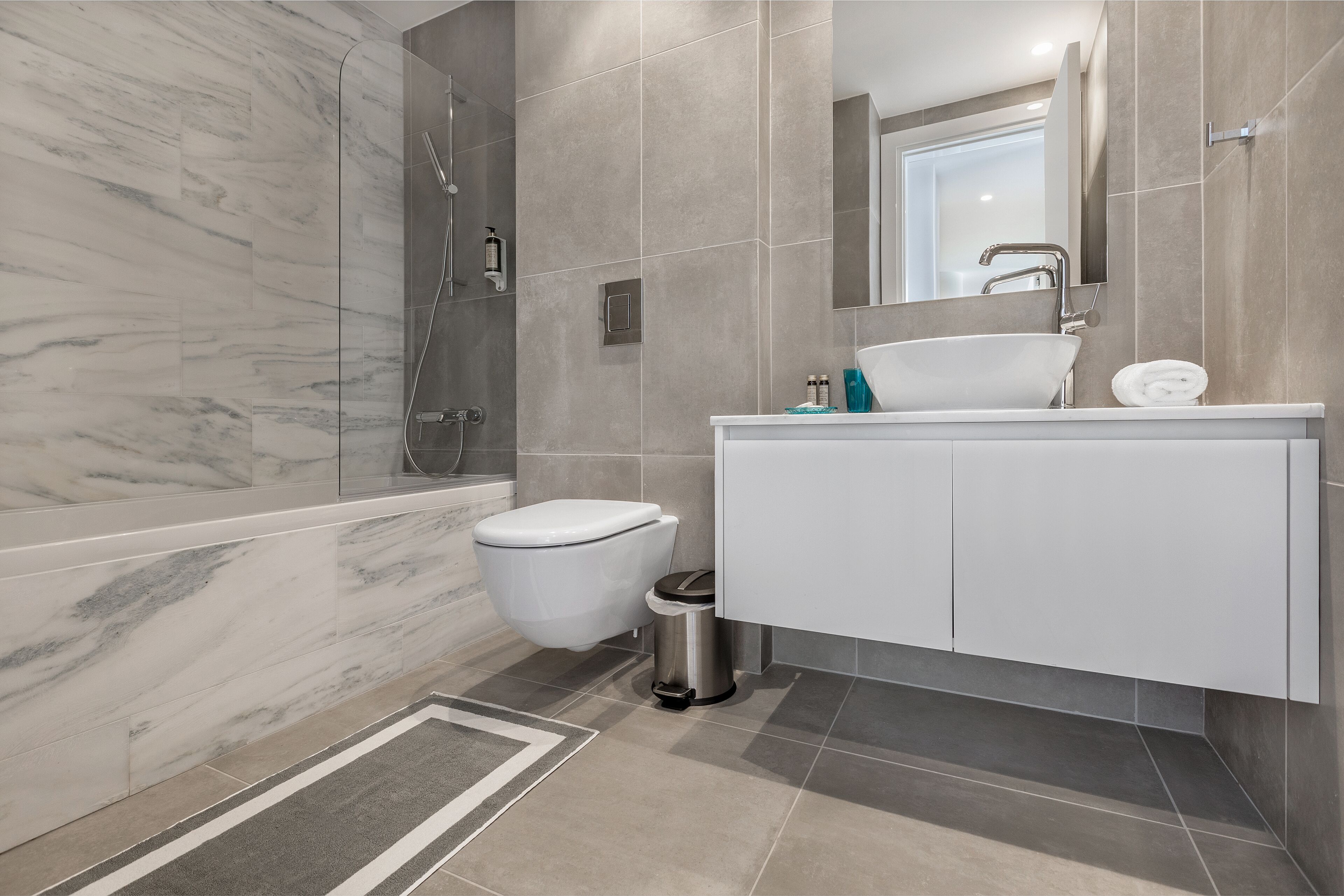 A modern bathroom with a marble shower, a toilet, a sink, and a trash can.