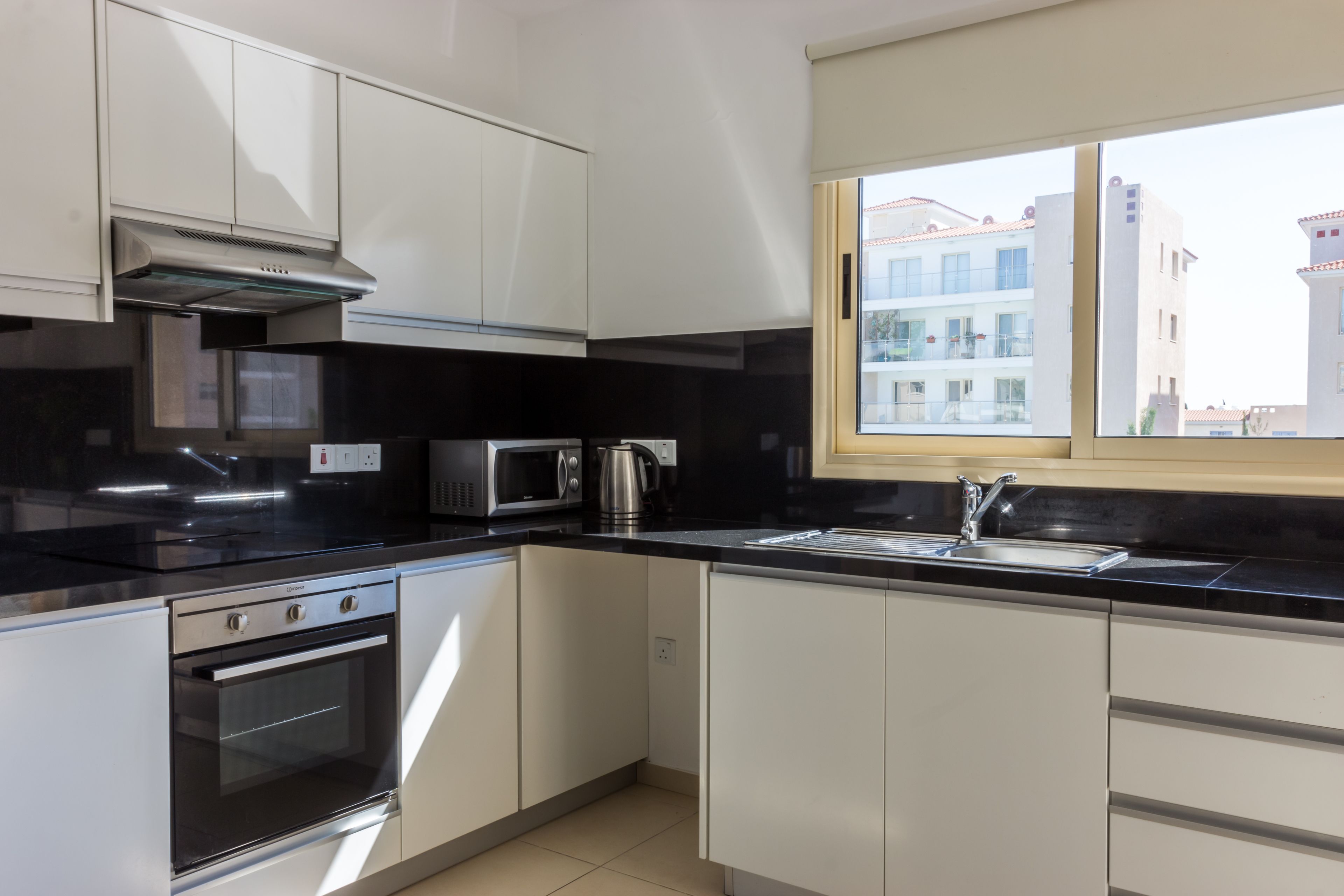 A modern kitchen with white cabinets, a black countertop, a built-in oven, a microwave, and a window with a view of buildings.