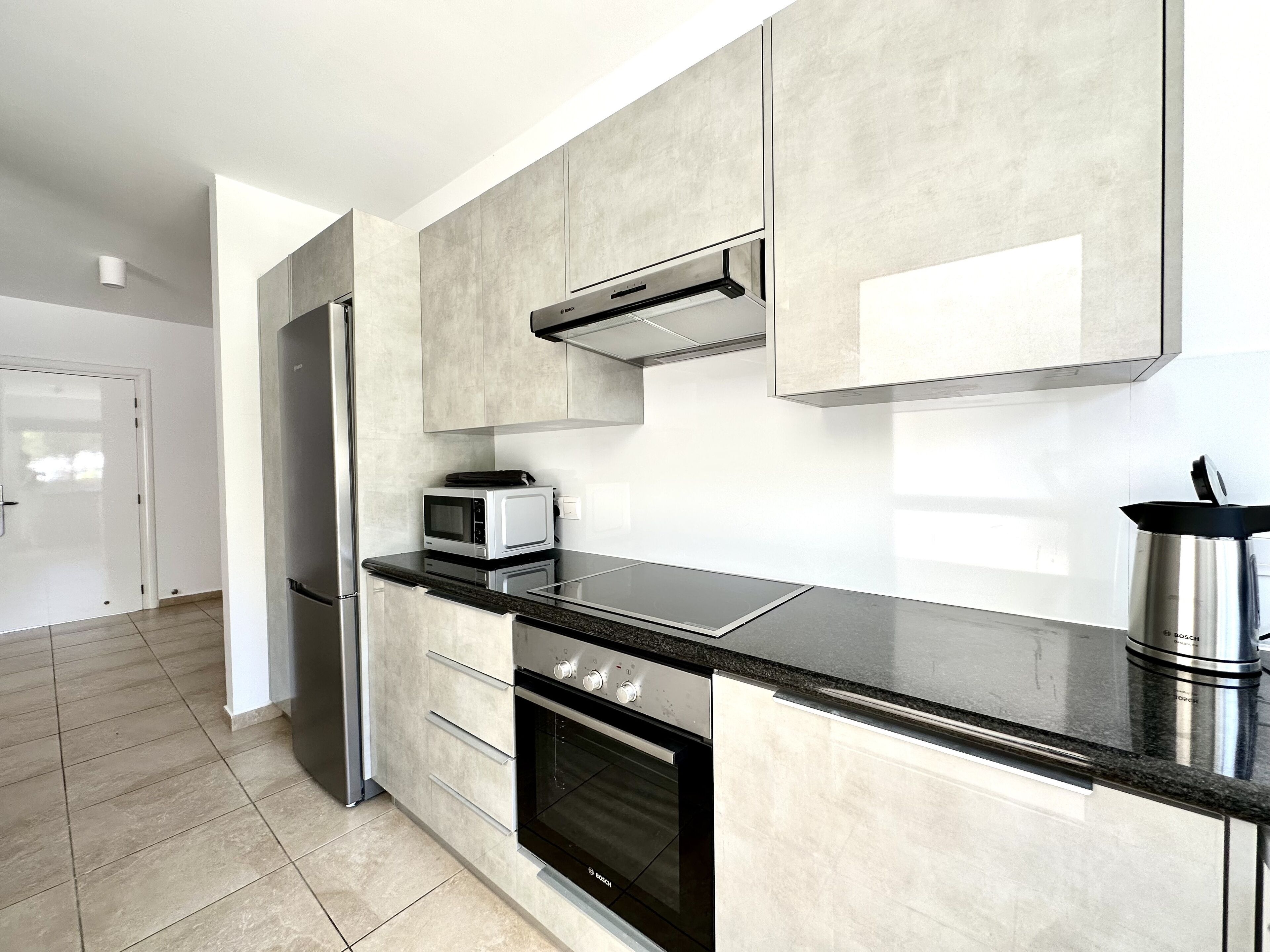 A modern kitchen with a stainless steel refrigerator, a Bosch microwave, a built-in oven, and a black countertop.