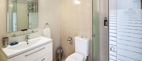 A modern bathroom with a glass shower enclosure, a white sink with a mirror above, and a toilet with a paper towel dispenser.