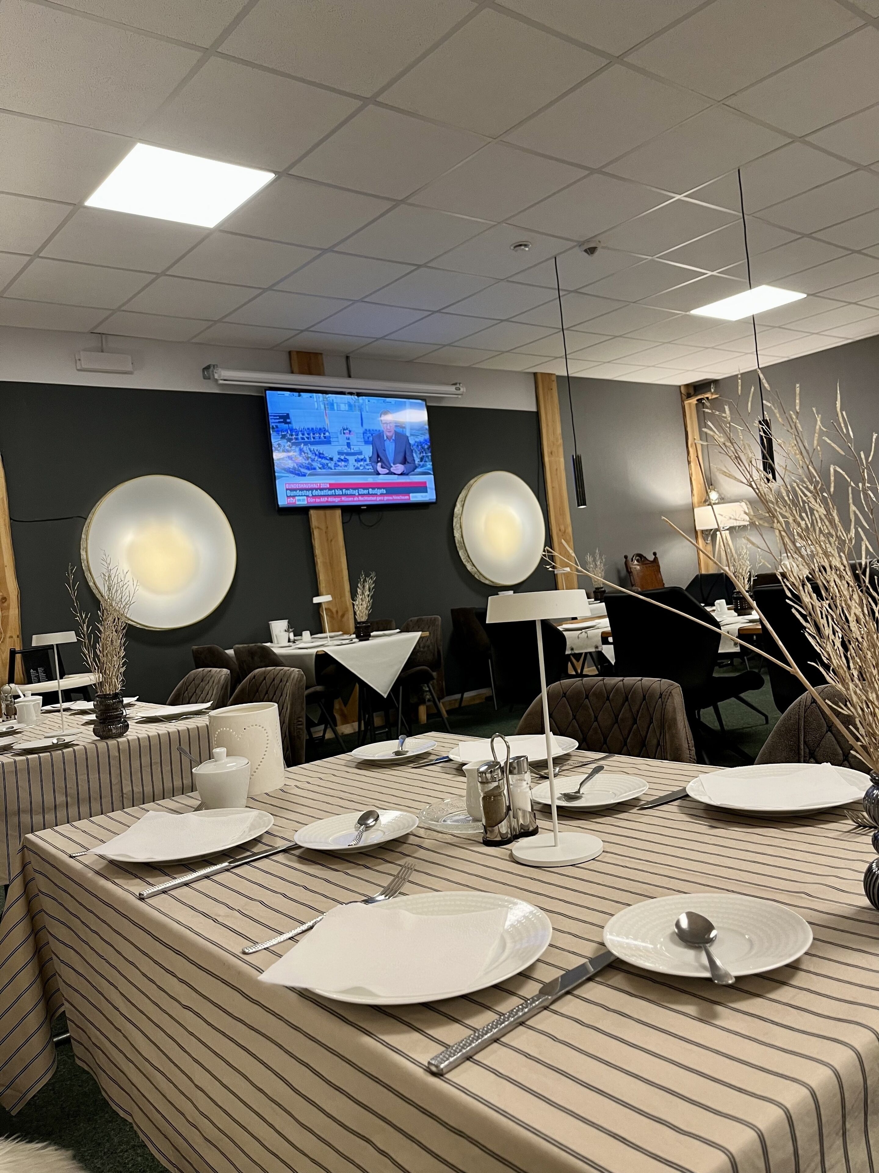 A conference room with a large table set for a meeting, a television screen displaying a news program, and a modern interior design.