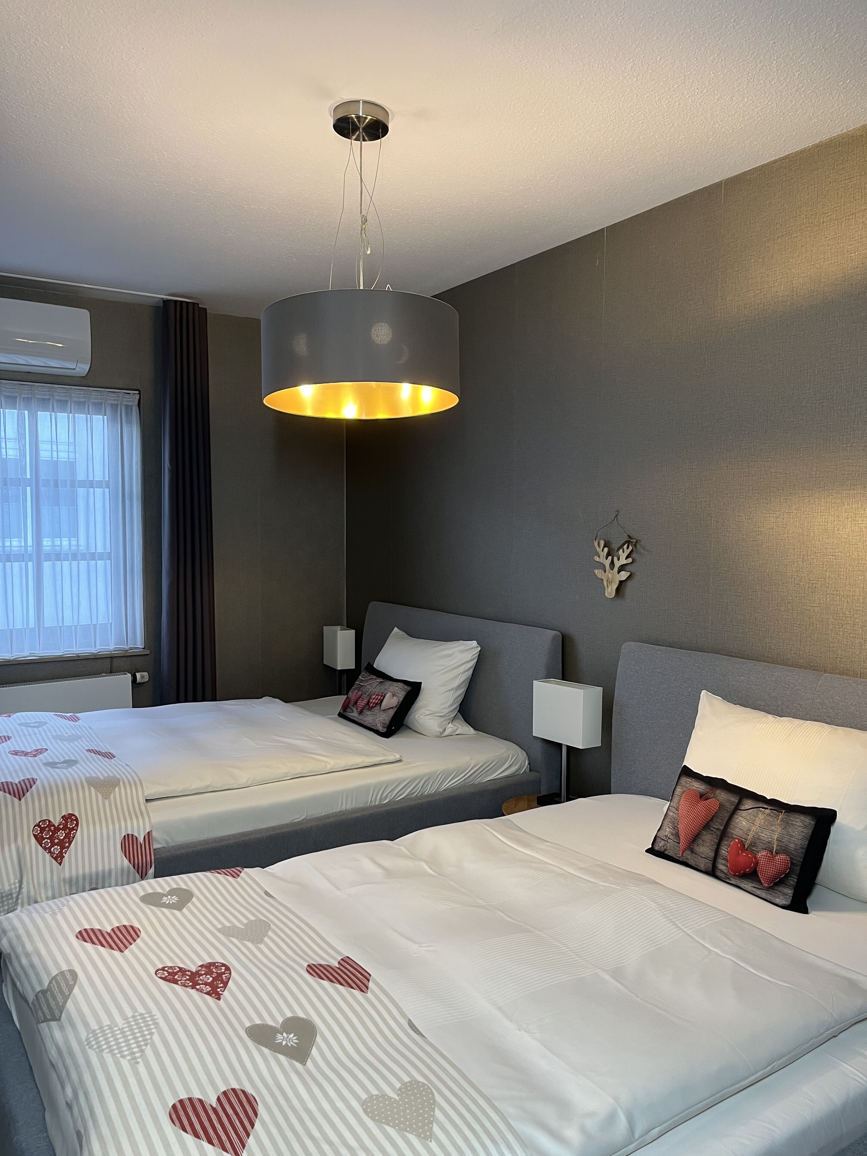 Een hotelkamer met twee bedden, een moderne kroonluchter en een decoratief wandobject.