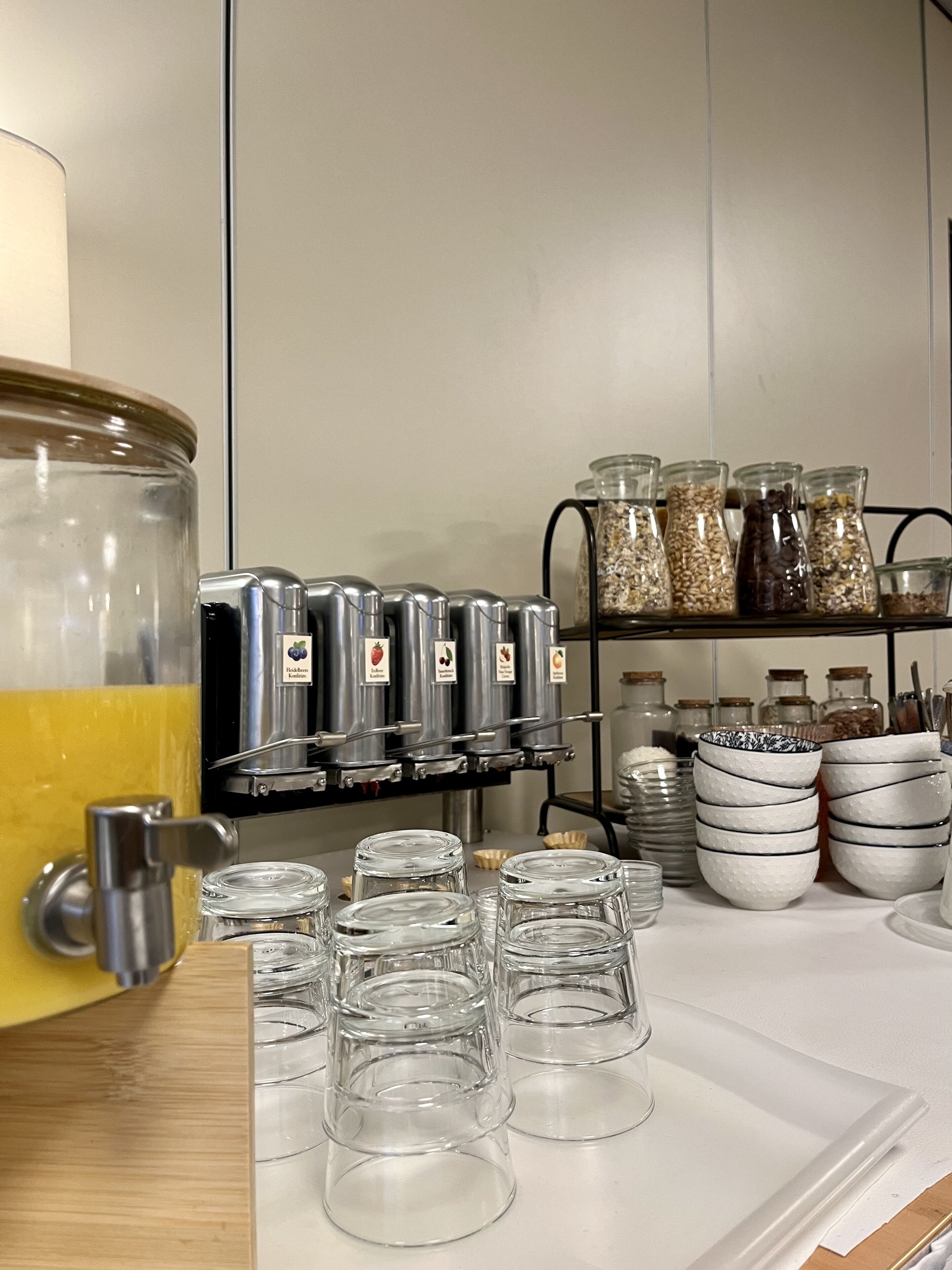 A breakfast bar with a large fruit punch container, multiple coffee dispensers, and a variety of food containers and bowls.