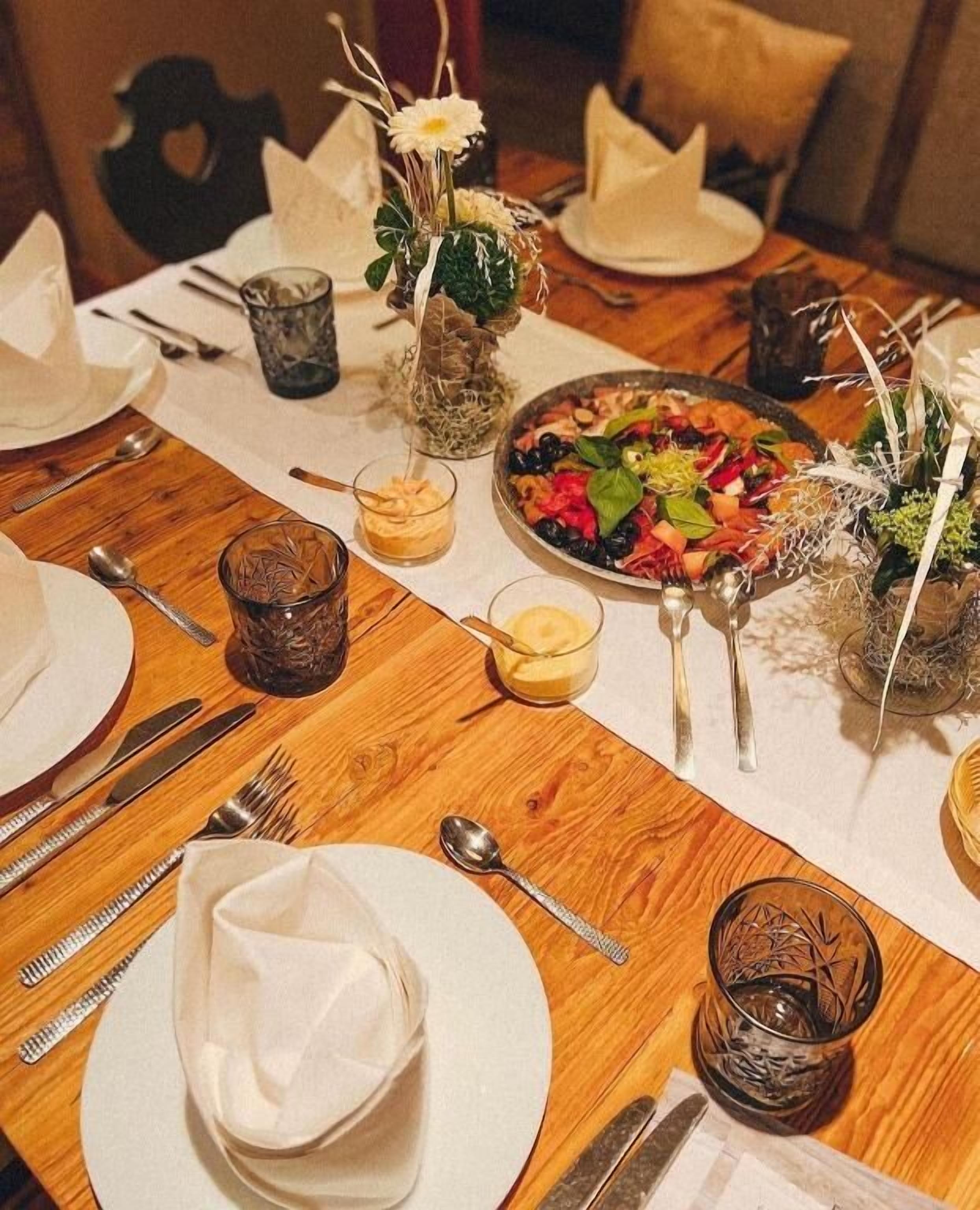 Una mesa de comedor dispuesta con platos, cubiertos, vasos y un plato principal.