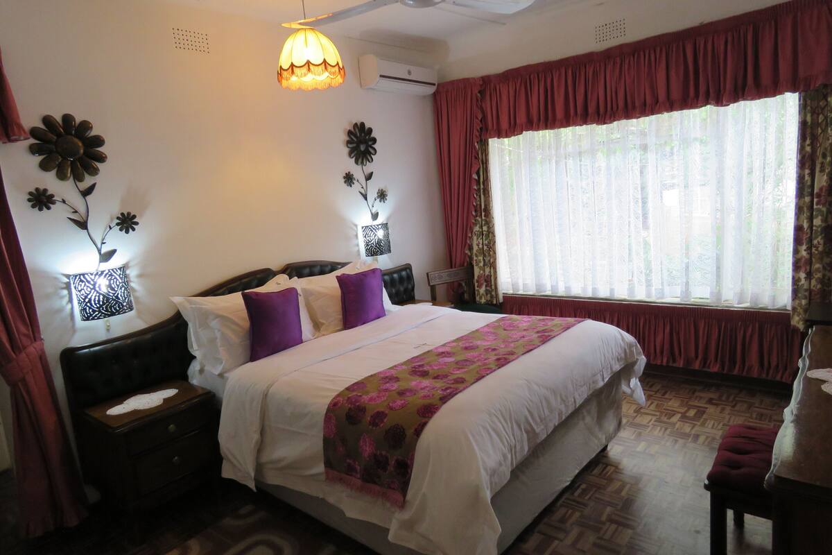 A bedroom with a large bed, a ceiling fan, a window with curtains, and wall-mounted flower decorations.