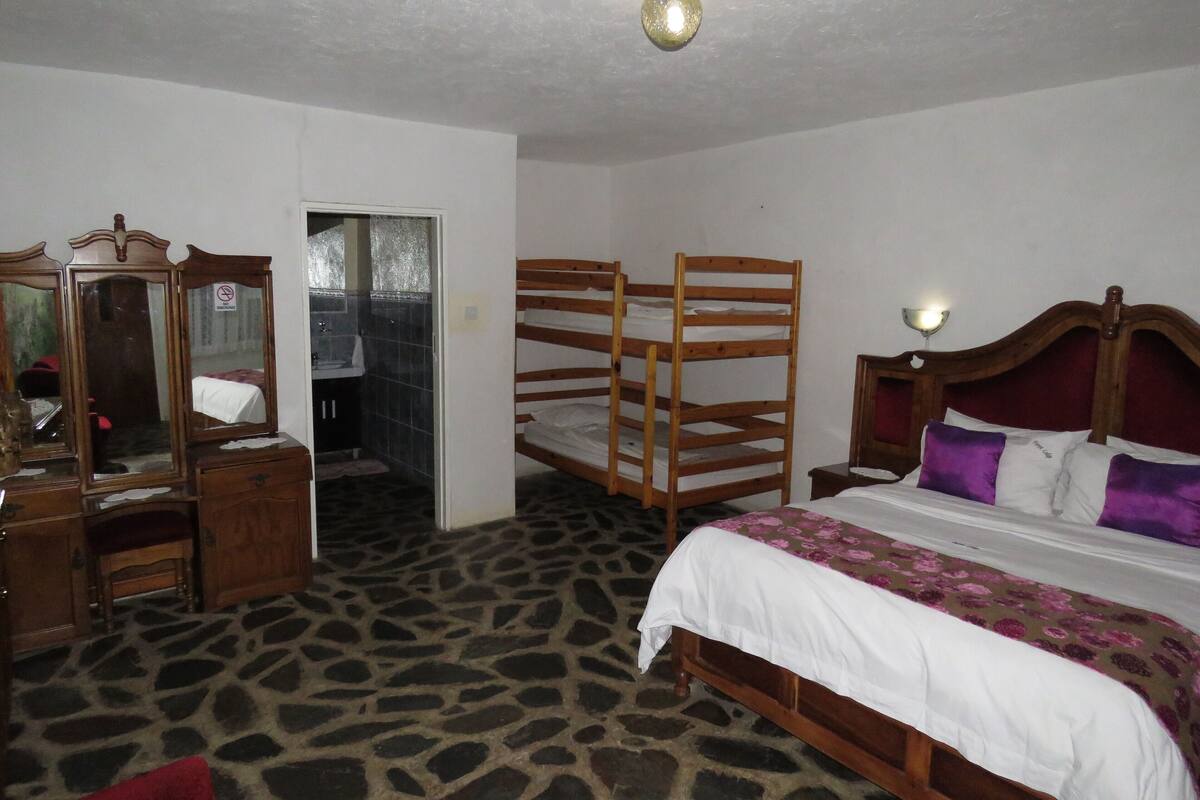 A bedroom with a bunk bed, a wooden dresser, a mirror, and a bathroom visible through an open door.