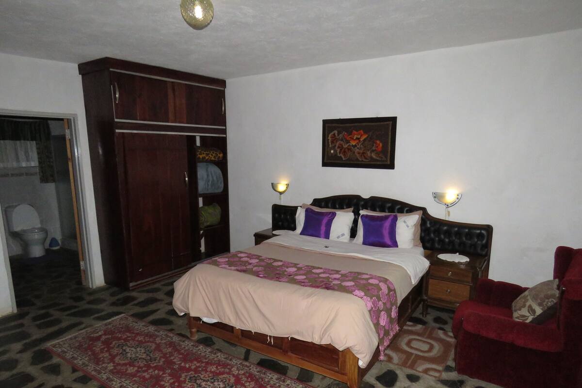 A bedroom with a bed, a wardrobe, a nightstand, a chair, and a painting on the wall.