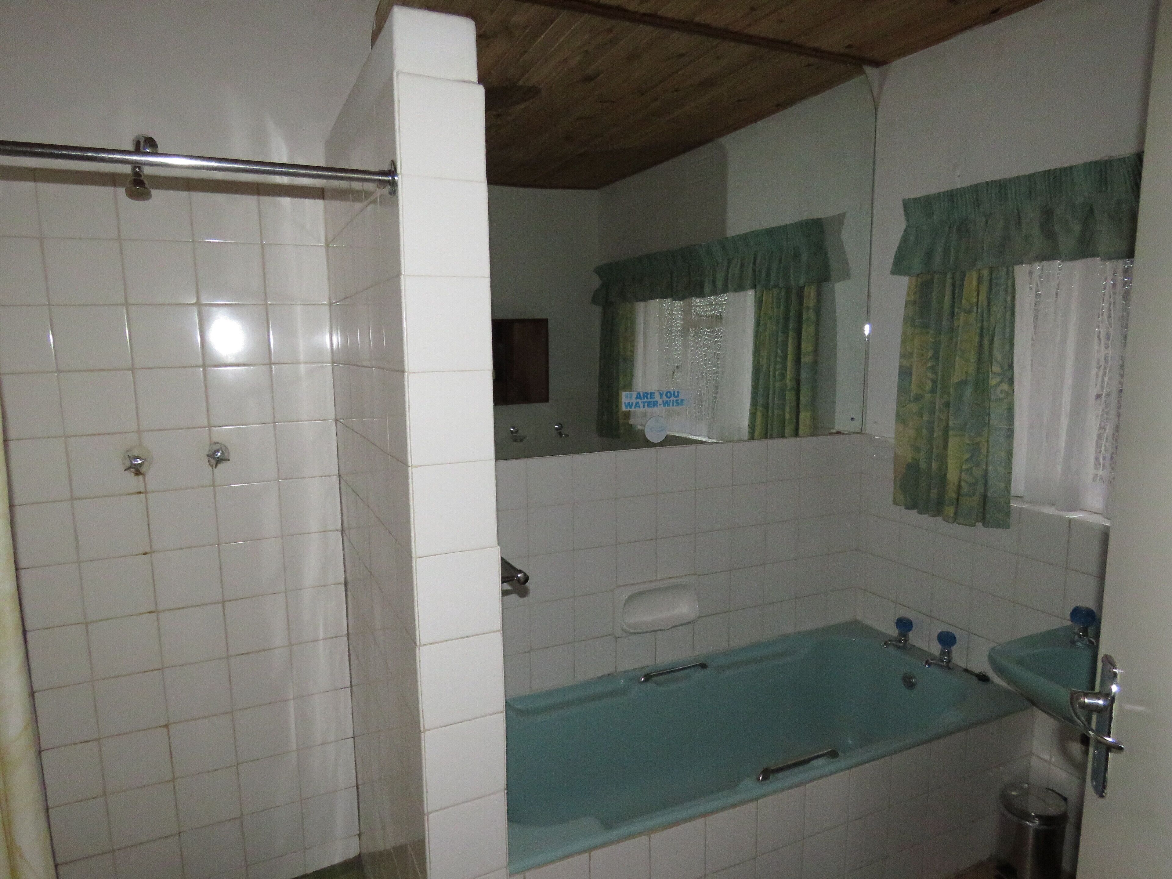 Ein Badezimmer mit weißen Fliesen, einer Badewanne, einer Dusche, einem Waschbecken und einem Spiegel.