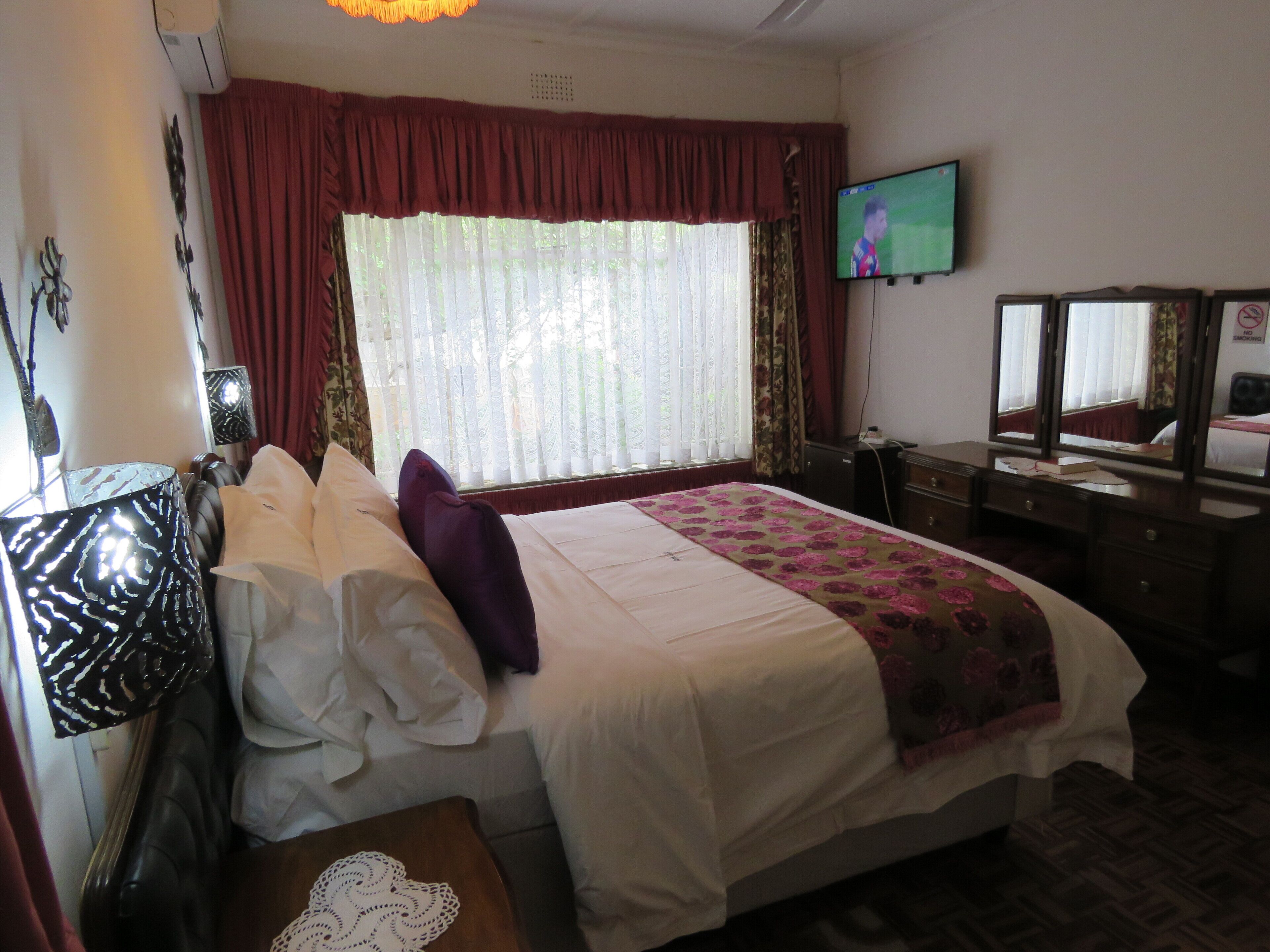 A hotel room with a bed, a television, a desk, and a window with curtains.