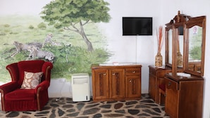 A room with a red armchair, a wooden cabinet, and a wall-mounted TV. - Parrot Lodge (Bulawayo)