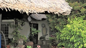 A rustic building with a thatched roof, a reception area, and a garden with various plants and flowers. - Parrot Lodge (Bulawayo)