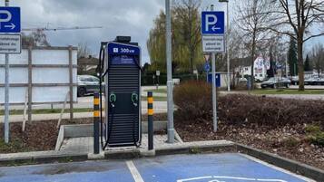 A parking area with electric vehicle charging stations, marked by blue signs with a white 'P' and arrows indicating the direction of the parking.