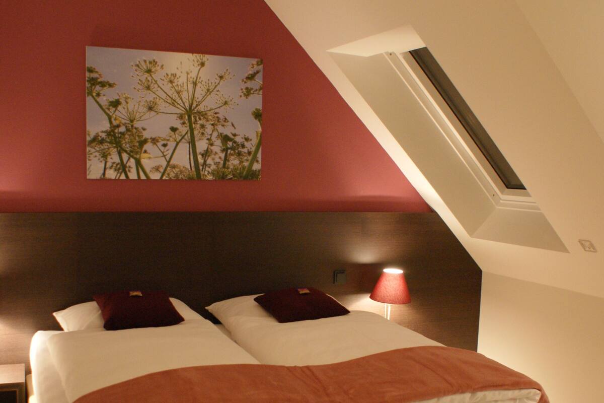 A bedroom with a large bed, a nightstand, a lamp, and a painting on the wall.