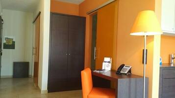 Quarto de hotel com escrivaninha, cadeira, abajur, telefone e guarda-roupa.