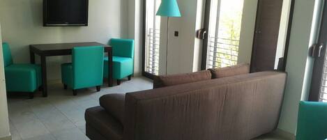 A living room with a brown sofa, teal chairs, a small table, and a TV mounted on the wall.