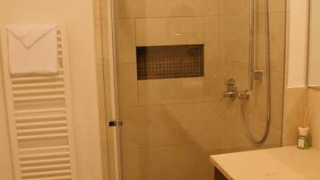 A bathroom with a glass-enclosed shower, a towel hanging on a radiator, and a small bottle of toiletries on the counter.