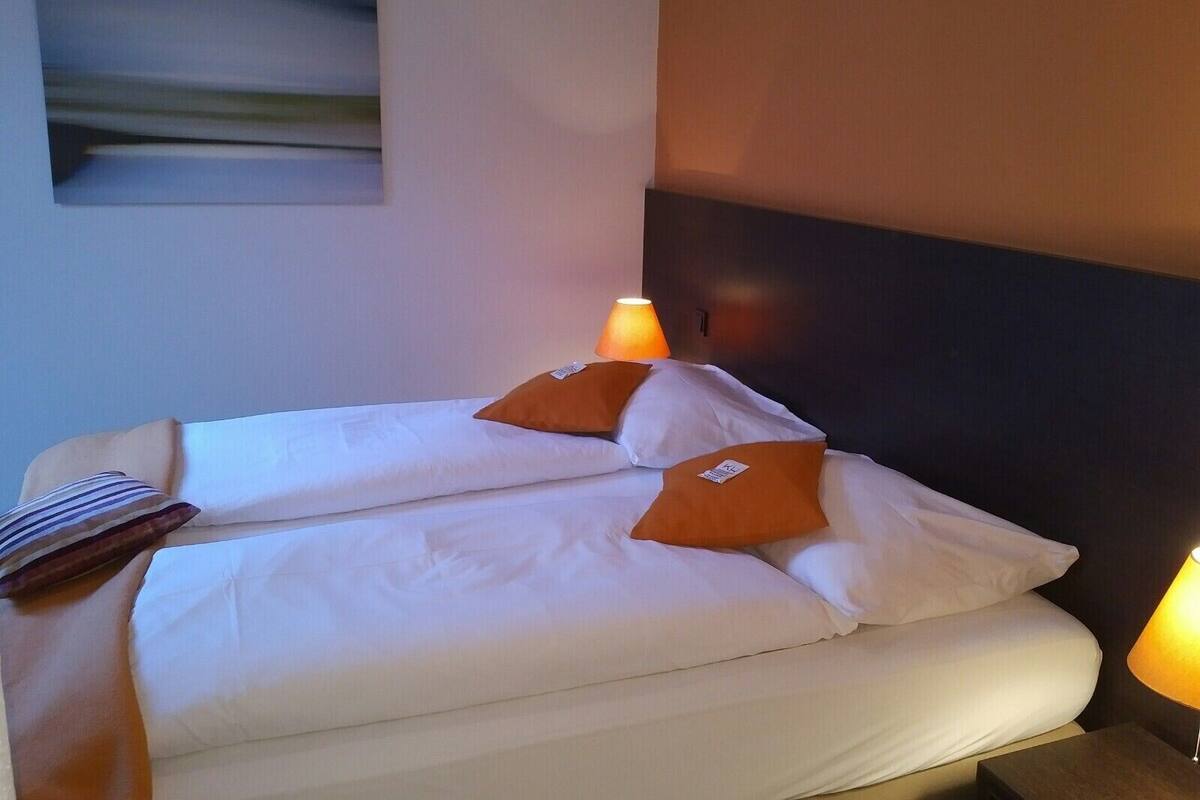 A hotel room with a bed, pillows, a lamp, and a painting on the wall.