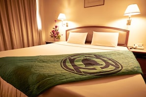 Una camera d'albergo con un letto rifatto, due lampade da comodino, un'composizione floreale e una coperta verde con motivo circolare.