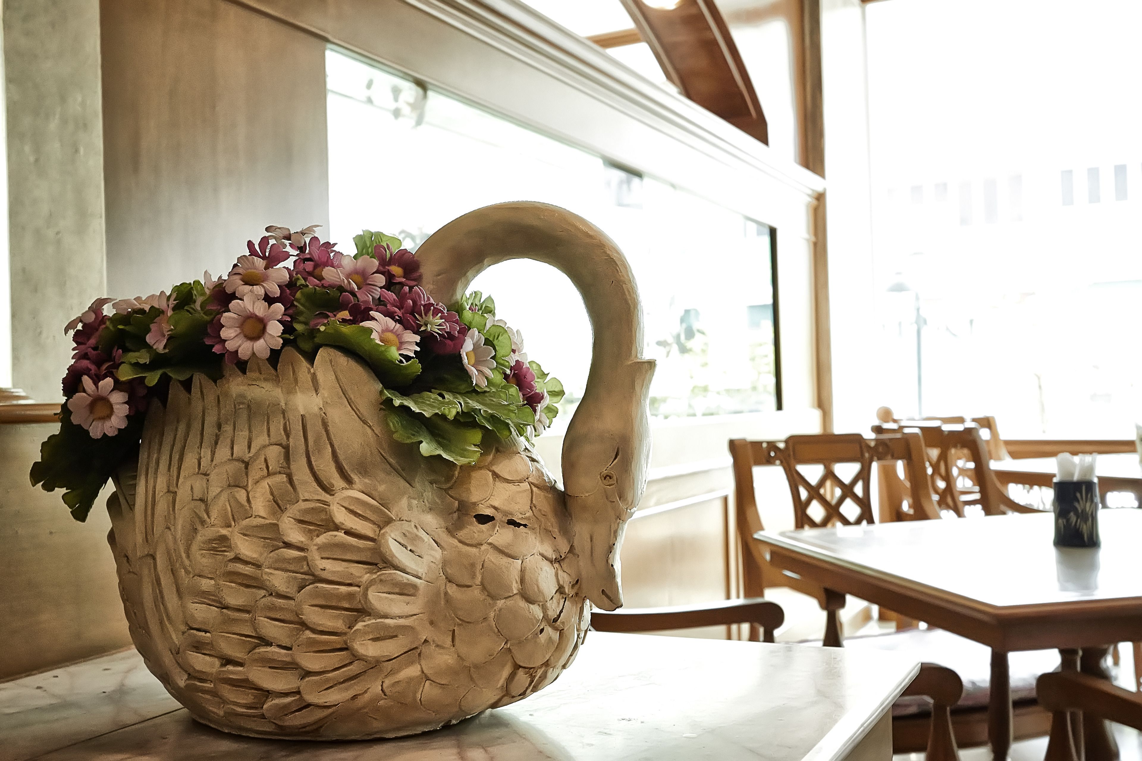A large ceramic swan-shaped vase with flowers on a table in a well-lit room with wooden furniture.